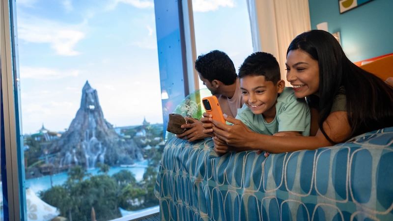 A happy family of three relaxing in their hotel room at Cabana Bay Beach Resort overlooking Volcano Bay.