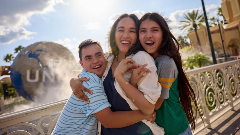 A family of three smiling and embracing as they pose for a photo together in front of the iconic Universal globe.
